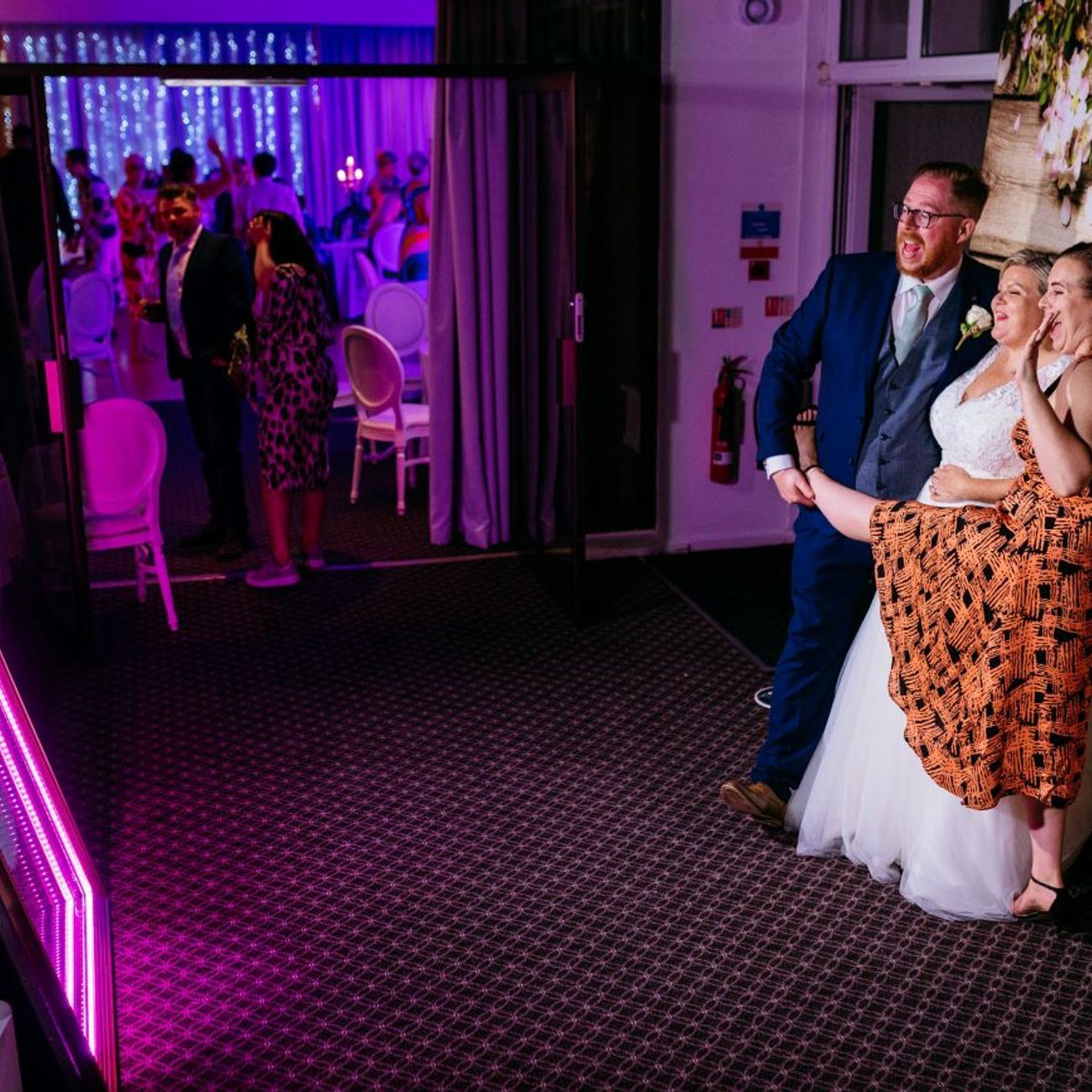 Bride and groom posing at the magic mirror with the pink-LED frame fully illuminated, captured photo preview visible on the mirror's screen