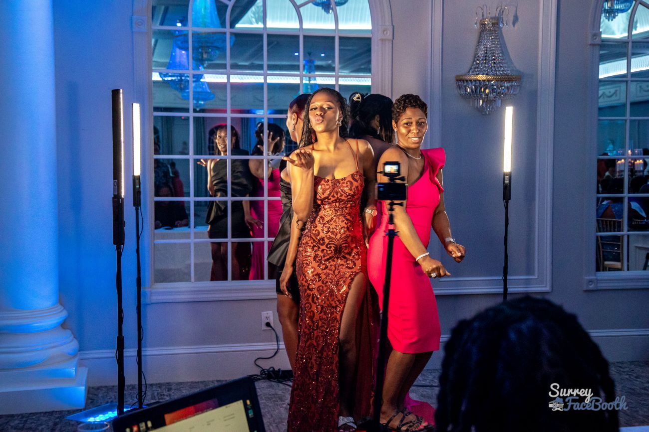 Two guests in evening dresses posing dramatically on the 360 video booth platform at a glamour event with LED light tubes flanking them