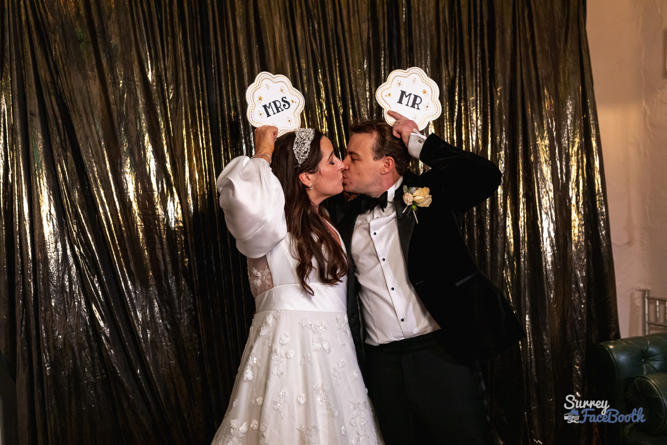 The bride and groom posing for photos in front of a backdrop, using props and sign boards